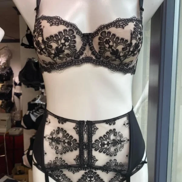 A black lace lingerie set displayed on a mannequin, featuring an underwire bra with detailed black floral lace and a matching high-waisted garter belt with intricate lace patterns. The garter belt includes straps for attaching stockings, creating a vintage-inspired, elegant look.